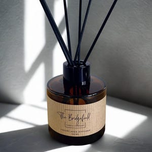 May include: A brown glass reed diffuser with black reeds. The bottle has a black cap and a label that reads "The Bridgefield Candle Company Luxury Reed Diffuser 100ml."