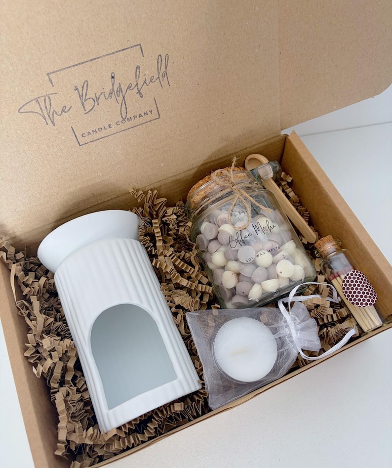 May include: A gift box from The Bridgefield Candle Company containing a white ribbed ceramic wax warmer, a glass jar filled with Coffee Mocha soy wax melts, a small wooden scoop, a white tea light candle in a mesh bag, and a glass vial of matches.