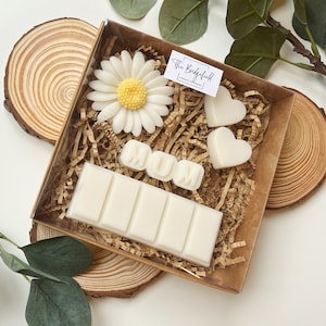 May include: A gift box filled with white wax melts, including a bar with multiple sections, two heart shapes, and a flower. The box also includes a white wax melt spelling out "MUM". The box is sitting on a wooden surface.
