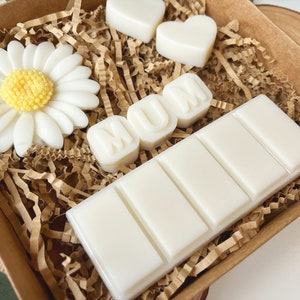 May include: A brown box filled with white wax melts. The melts are shaped like a daisy, hearts, and the word "MUM".