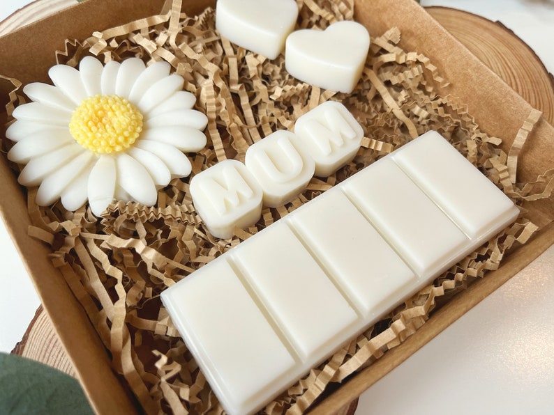 May include: A brown box filled with white wax melts. The melts are shaped like a daisy, hearts, and the word "MUM".