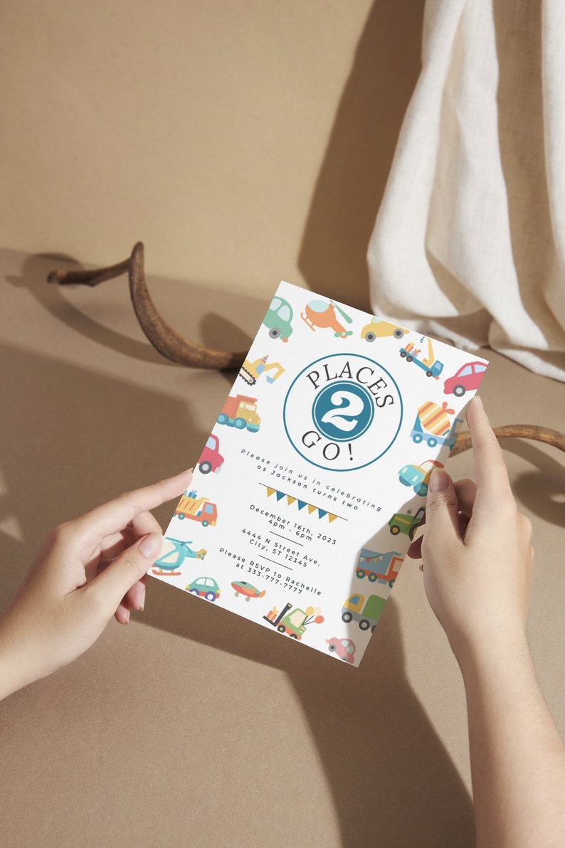May include: A white invitation card with a blue circle that says "Places 2 Go!" and has a number 2 in the center. The card is decorated with colorful illustrations of vehicles, including trucks, cars, helicopters, and construction equipment. The text on the card reads "Please join us in celebrating as Jackson turns two. December 16th, 2023, 4pm - 6pm, 4444 N Street Ave., City, ST 12345. Please RSVP to Rachelle at 333-777-7777."