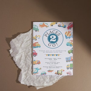 May include: A colorful invitation for a second birthday party with a Places 2 Go! theme. The invitation features a blue circle with the number 2 and the words Places 2 Go! surrounded by illustrations of vehicles, including a helicopter, a truck, a car, and a construction vehicle. The invitation also includes the date, time, and location of the party, as well as an RSVP request.