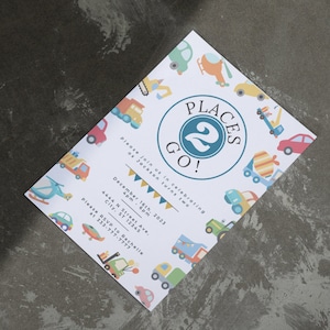 May include: A white invitation with a blue circle that says "Places 2 Go!" with a number 2 inside the circle. The invitation is decorated with colorful cartoon vehicles and the text "Please join us in celebrating as Jackson turns two. December 16th, 2023 4pm - 6pm 4444 N Street Ave. City, ST 12345 Please RSVP to Rachelle at 333-777-7777"