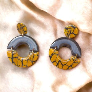 Könnte beinhalten: Ein Paar schwarze und goldene Statement-Ohrringe mit einer craquelé-Glasur. Die Ohrringe sind rund und haben einen großen, offenen Kreis in der Mitte.