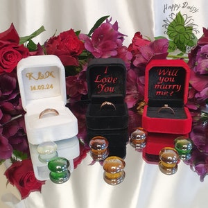 May include: Three velvet ring boxes with different embroidery. The white box says "K&M 14.02.24", the black box says "I Love You", and the red box says "Will you marry me?"