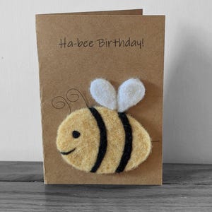May include: A brown card with the text "Ha-bee Birthday!" and a felt bee with black stripes and white wings.