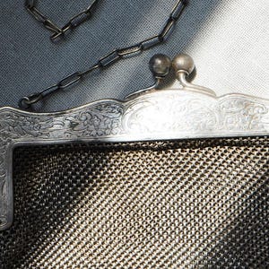 May include: Close-up of a vintage silver mesh purse with a chain handle. The purse has a decorative floral design on the frame and a clasp with two round ball details. The mesh is a fine, woven pattern.