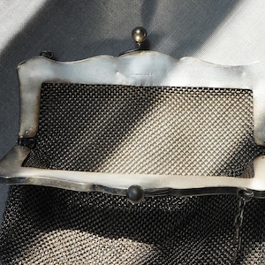 May include: A vintage silver mesh purse with a decorative frame. The purse features a fine, woven mesh body and a silver frame with a scalloped edge. A small, round clasp secures the purse.