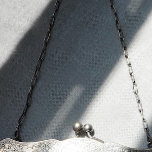 May include: Close-up of a vintage silver mesh purse with a decorative floral design on the frame. The purse has a chain handle and a clasp closure with two small, round silver balls. The mesh is a dark, woven pattern.