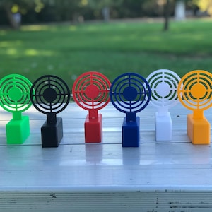 May include: A row of six colorful, miniature fan-shaped objects. Each fan has a circular design with concentric rings and is mounted on a rectangular base. The fans are in green, black, red, blue, white, and orange.