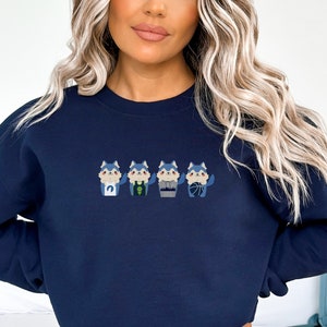 May include: A navy blue sweatshirt with a graphic of five cartoon wolves wearing different outfits. The wolves are all blue with white accents and are standing in a row.