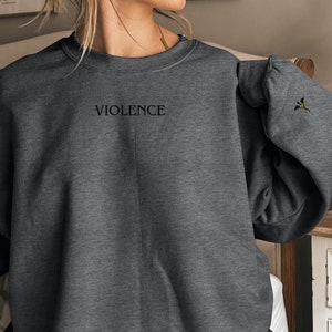Może przedstawiać: Szara bluza z kapturem z napisem "VIOLENCE" wyszytym z przodu. Bluza ma mały haft na prawym rękawie.