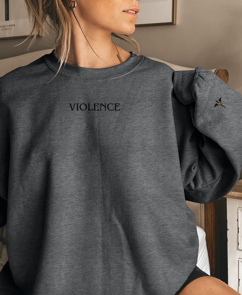 Może przedstawiać: Szara bluza z kapturem z napisem "VIOLENCE" wyszytym z przodu. Bluza ma mały haft na prawym rękawie.