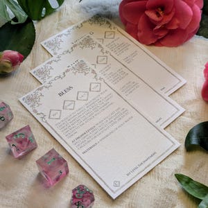 May include: A white card with the words "Bless" and "30ft" printed on it. The card is decorated with a floral design and has a light pink background. The card is part of a set of cards that are used for a role-playing game.