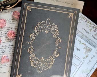 May include: A black hardcover book featuring a gold foil ornate frame design on the front cover. The book is surrounded by pink translucent polyhedral dice, a sheet of paper with handwritten cursive text, and a combat tracker card.