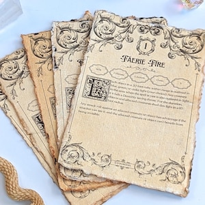 May include: A stack of aged paper cards with ornate black border designs and text. The top card reads "FAERIE FIRE" with game instructions. Several iridescent dice and a carved snake figurine are in the background.