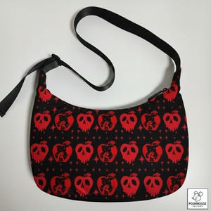 May include: Black shoulder bag with a repeating pattern of red apple-skull designs. The bag has a black adjustable strap and a zipper closure. The bag is made of a durable fabric and is suitable for everyday use.