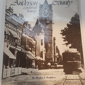 May include: A vintage book titled "Anderson County a pictorial history" with a sepia-toned image of a town square and a trolley car. The author's name, Hurley E. Badders, is printed at the bottom. The book cover is slightly worn.