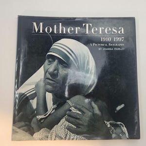 May include: A black and white hardcover book titled Mother Teresa 1910-1997 A Pictorial Biography by Joanna Hurley. The cover features a photograph of Mother Teresa wearing her signature white head covering with blue stripes, holding a small child.