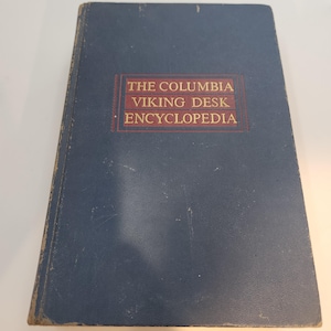 May include: A vintage blue hardcover book titled "The Columbia Viking Desk Encyclopedia." The title is in a red rectangular box on the front cover. The book shows signs of wear.