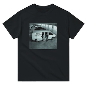 May include: Black t-shirt featuring a graphic print of a white van with the text "FREE KETAMINE" and two figures in white robes and hoods. The image is a grayscale photograph.