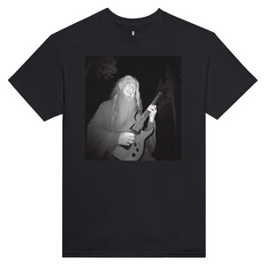 Könnte beinhalten: Schwarzes T-Shirt mit einem Schwarz-Weiß-Bild einer langhaarigen, bärtigen Person, die eine E-Gitarre spielt. Das Bild ist vor einem dunklen Hintergrund, möglicherweise einem Wald, platziert. Das T-Shirt hat einen Rundhalsausschnitt und kurze Ärmel.