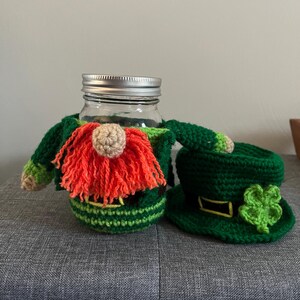 Peut inclure: Un couvre-jarre et un chapeau de gnome lutin en crochet. Le gnome a un chapeau vert et jaune, un corps vert et jaune et une barbe rouge. Le chapeau est vert avec une bande jaune et un trèfle vert.