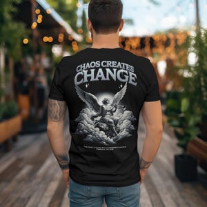 May include: Black t-shirt with a graphic of an angel playing a trumpet in the clouds. The text "Chaos Creates Change" is printed above the angel. The text "The night is dark, but chaos brings change. Embrace the dawn" is printed below the angel.