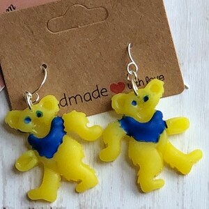 May include: A pair of yellow bear-shaped earrings with blue accents. The earrings are handmade and come on silver hooks.