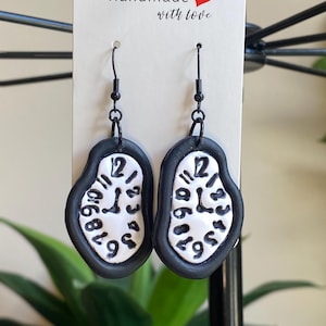 May include: A pair of black and white earrings featuring a melted clock design. The earrings are made of polymer clay and have a black hook.