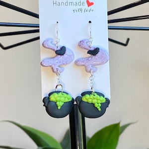 Op de afbeelding: Paarse en zwarte glitter-geest oorbellen met een zwarte ketel bedel met groene accenten. De oorbellen zijn handgemaakt met liefde.