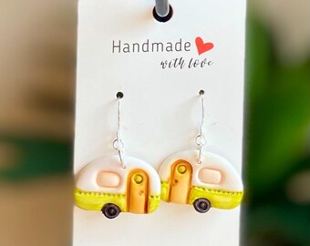 May include: A pair of dangle earrings featuring a white and yellow camper van design with green trim. The earrings are handmade with love.
