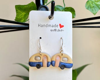 May include: A pair of blue and yellow camper van earrings with silver hooks. The earrings are handmade and have the text "Handmade with love" on the card they are displayed on.
