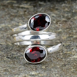 May include: A silver ring featuring two red oval-shaped gemstones. The ring has a twisted band design.
