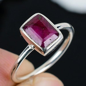 May include: A silver ring featuring a rectangular ruby gemstone. The ring has a simple band and the ruby is a deep red colour.