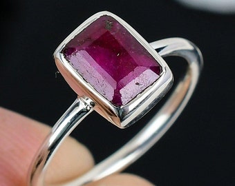 Puede incluir: Un anillo de plata con una piedra preciosa de rubí rectangular. El anillo tiene una banda simple y el rubí es de color rojo intenso.