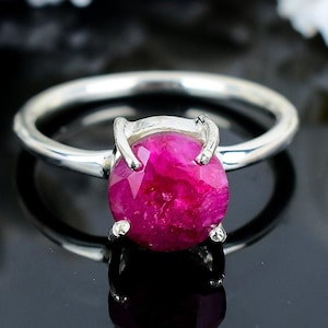 May include: A silver ring featuring a large, round, pink ruby gemstone set in a prong setting.