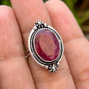 May include: A silver ring with a large oval-shaped red gemstone set in a decorative silver bezel. The ring is on a finger.