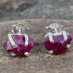 May include: A pair of sterling silver earrings featuring raw ruby gemstones. The earrings are marked with "925" on the back.