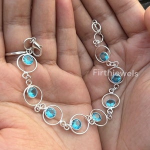 May include: A silver bracelet featuring a chain of interlinked circles, each circle set with a light blue gemstone. The bracelet has a lobster clasp.