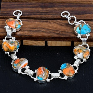 May include: A silver bracelet featuring six oval-shaped turquoise and coral stones. The stones are set in silver and the bracelet has a chain link design.