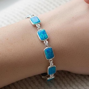 Peut inclure: Un bracelet en argent orné de pierres d'opale bleues rectangulaires et vibrantes. Le bracelet est composé d'une série de pierres d'opale reliées par des connecteurs en argent. Les opales ont une qualité chatoyante et irisée.