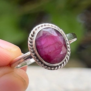 May include: A silver ring featuring a pink oval ruby gemstone set in a twisted rope design band.