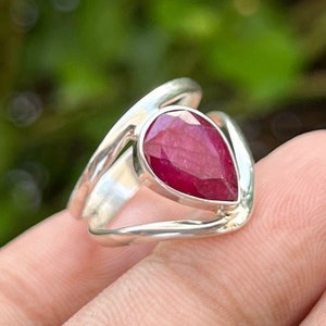 May include: A silver ring featuring a teardrop-shaped ruby gemstone. The ring has a delicate, twisted band.