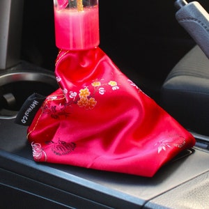 Puede incluir: Una palanca de cambios de coche rosa y dorada con un diseño floral en el interior. La palanca está cubierta de una tela de satén rosa con un patrón floral.