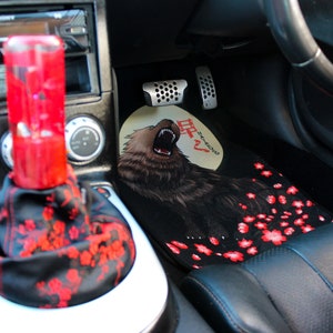 Puede incluir: Interior de coche negro con una alfombra personalizada que presenta un oso rugiente y flores de cerezo. La alfombra tiene la palabra japonesa "月" (luna) y el texto "Sakura".