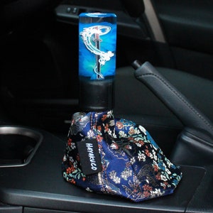 May include: A blue and white gear shift knob with a sword and wave design. The knob is attached to a blue and gold patterned gear shift boot with the word "HAYAKUCO" printed on it.