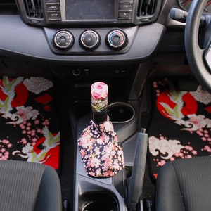 May include: Black car interior with a floral patterned gear shift boot and matching floor mats with a crane and cherry blossom design.
