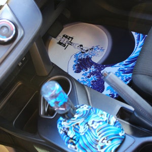 May include: A blue and white car interior with a custom gear shift knob and floor mat featuring a Japanese wave design.
